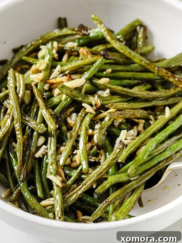 Roasted Green Beans with Almonds, garnished with fresh herbs and lemon wedges.