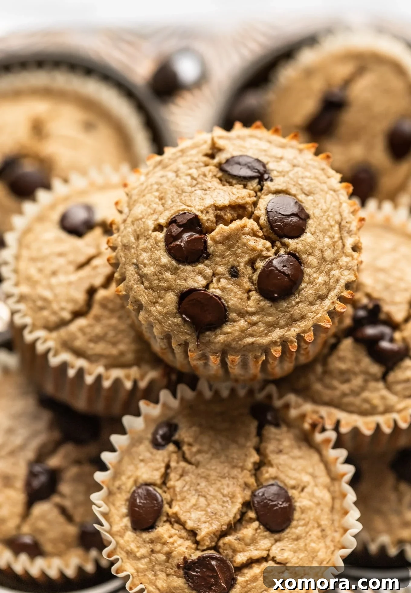 Golden Banana Oat Chocolate Chip Delights 2 A stack of golden brown chocolate chip banana oat muffins, with chocolate chips visible on top, presented on a rustic background.