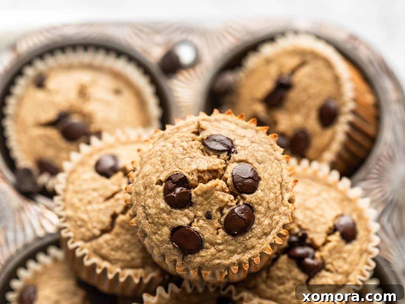 Golden Banana Oat Chocolate Chip Delights 4 A baking sheet filled with freshly baked chocolate chip banana oat muffins cooling, still in their muffin liners.