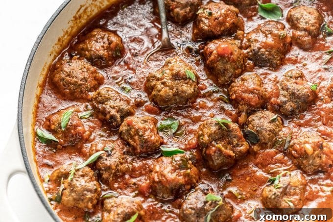 Slow-Simmered Marinara Meatballs 4 Cooked meatballs simmering in a rich, red marinara sauce in a cast iron skillet.
