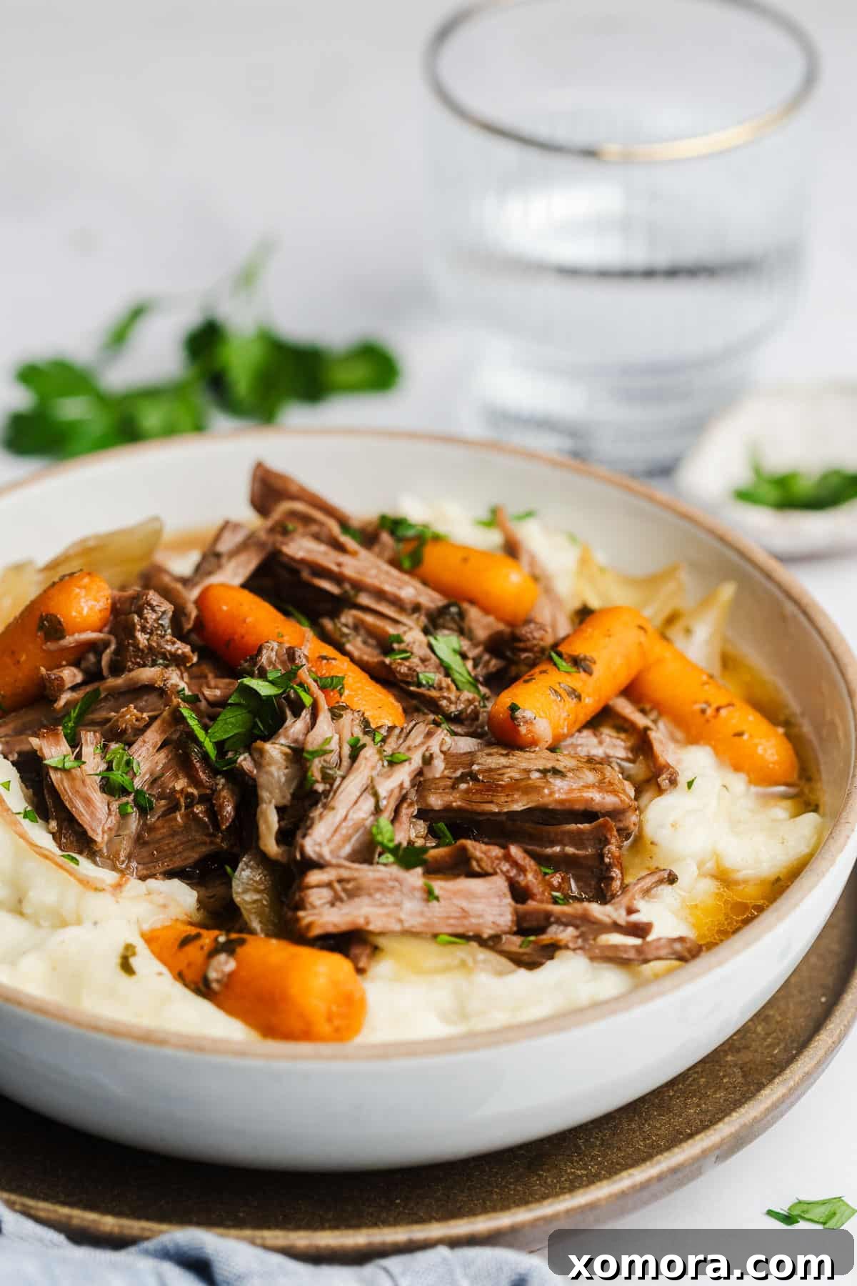 Effortless Slow Cooker Garlic Herb Pot Roast 6 A bowl of slow cooker garlic herb pot roast served over mashed potatoes, garnished with fresh herbs.