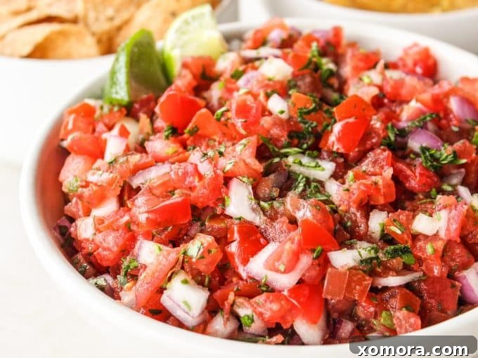 A bowl of Pico de Gallo, with some chips and fresh limes on the side.