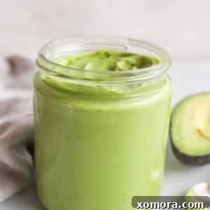 A perfectly ripe avocado, sliced, next to a bowl of creamy avocado dressing, ready for blending.