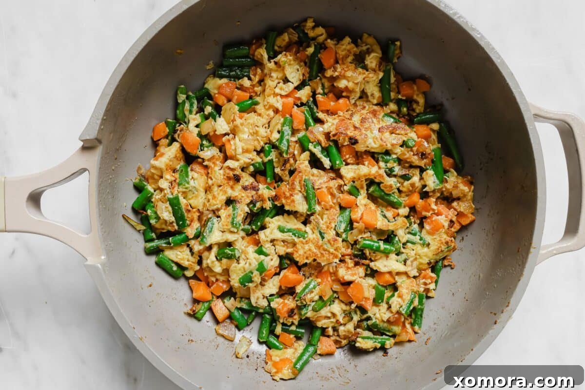 Wholesome Cauliflower Chicken Fried Rice 4 Various stages of cooking cauliflower chicken fried rice: chicken searing, vegetables sautéing, and eggs scrambling in a large skillet.