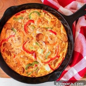 Round Chicken Sausage & Pepper Frittata in a cast iron skillet, with a slice removed to show the interior.