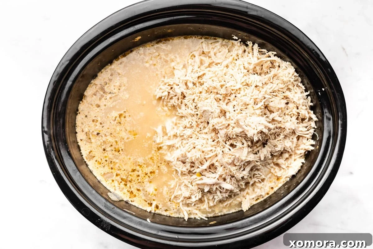 Close-up of Slow Cooker White Chicken Chili showing the creamy texture, corn, beans, and shredded chicken, with a spoon digging in.