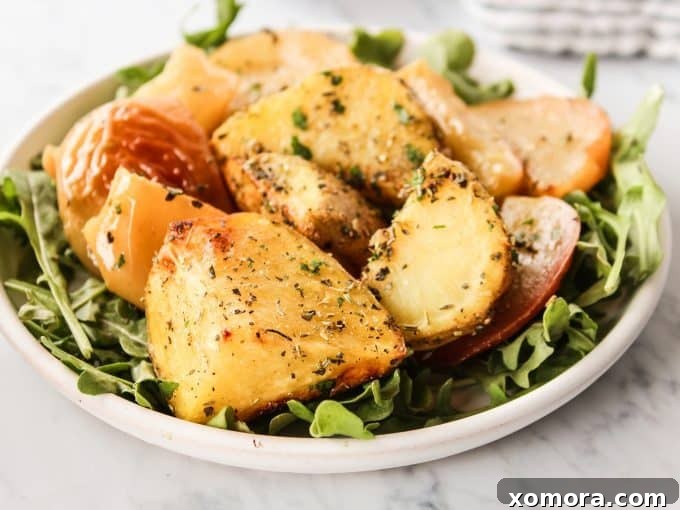 Sliced potatoes and apples tossed with herbs and oil on a sheet pan before roasting.