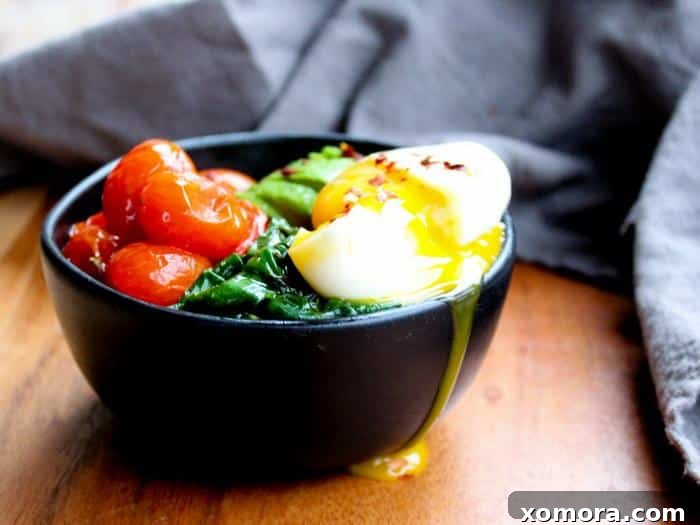 A horizontal shot of the healthy Poached Eggs & Garlic Spinach meal, garnished with avocado and roasted tomatoes.