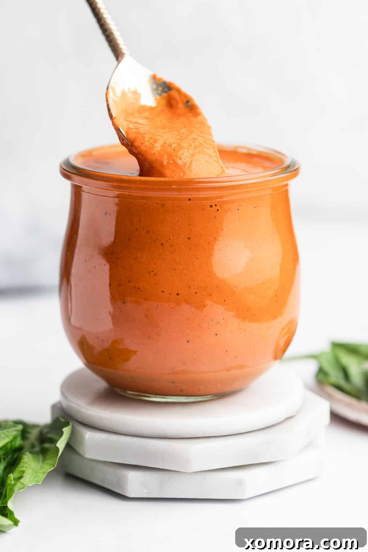 A vibrant, creamy roasted red pepper sauce in a bowl, garnished with fresh basil leaves, ready to be served.
