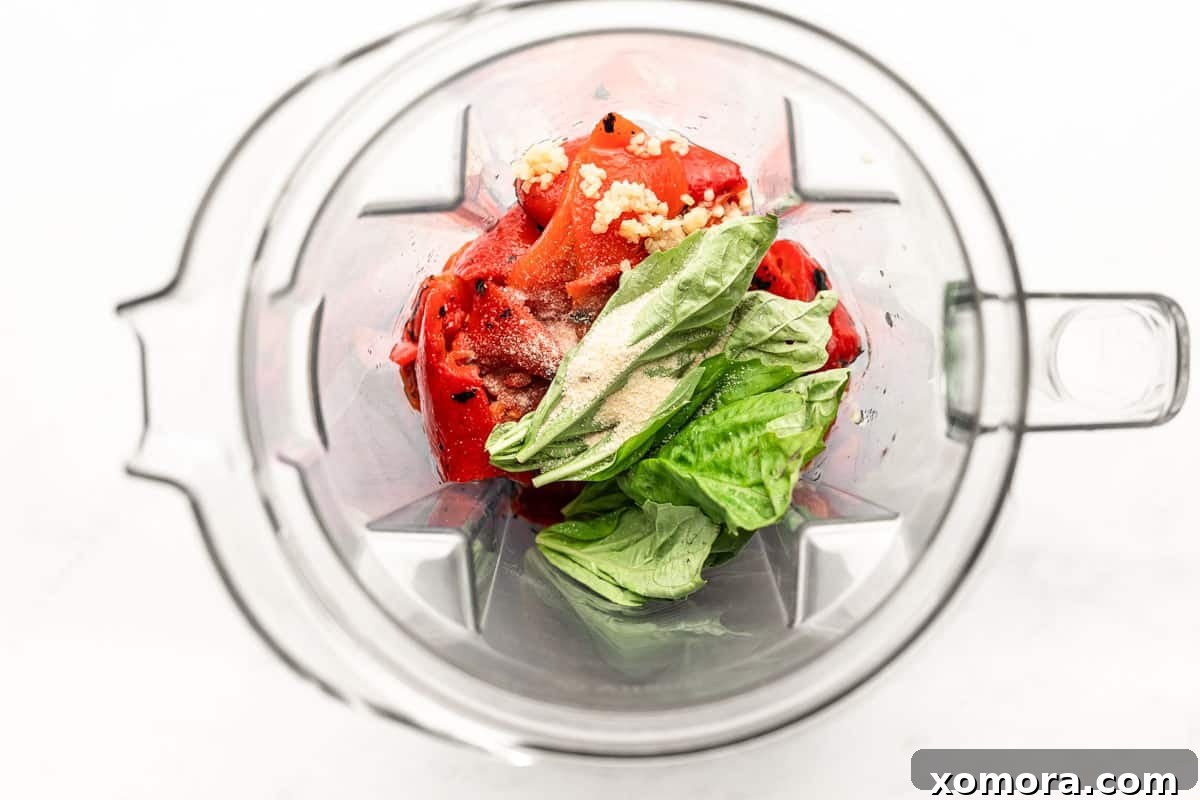 Fresh basil leaves and minced garlic, key ingredients for the roasted red pepper sauce, laid out next to a blender.