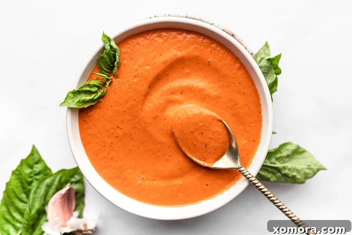 A close-up of creamy roasted red pepper sauce being drizzled over a dish, highlighting its rich, smooth texture.