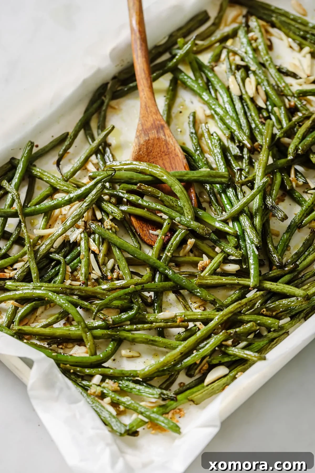 Crispy Roasted Green Beans & Toasted Almonds 5 A platter of golden brown roasted green beans with toasted almonds and lemon wedges.