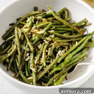 Close-up of a serving of roasted green beans with almonds, garnished with a lemon slice.