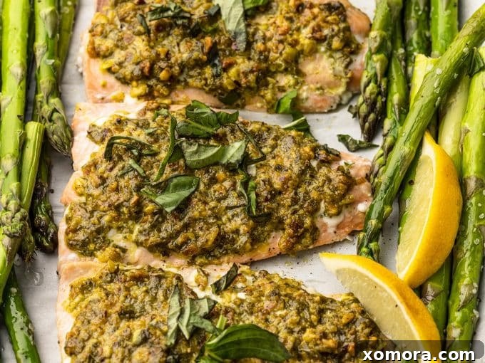 A sheet pan with four portions of cooked pistachio herb crusted salmon and roasted asparagus, ready to be served.