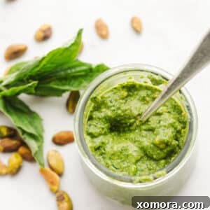 A small bowl of homemade dairy-free pistachio lemon pesto, garnished with a basil leaf.