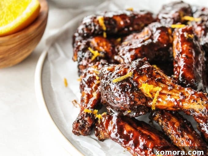 Zesty Orange Balsamic Glazed Wings 4 A serving of finished sticky orange balsamic wings in a bowl, with a sprig of fresh herb for garnish.