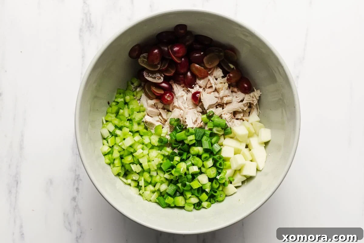 Close-up shot of the ultimate chicken salad ingredients mixed in a large bowl, highlighting fresh apples, grapes, and celery.