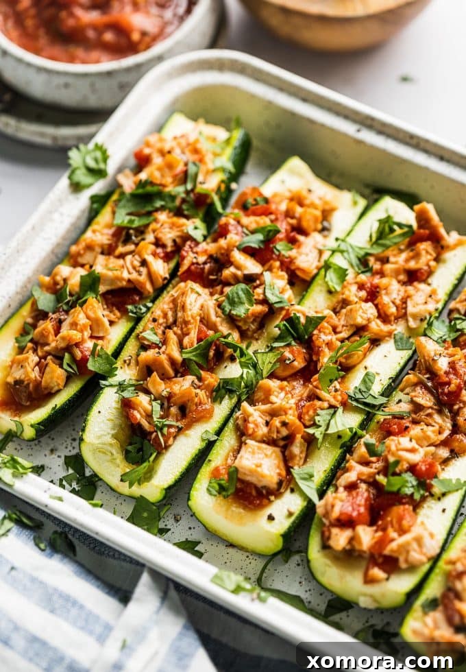 Fiesta Chicken Zucchini Boats 2 Two halves of cooked salsa chicken zucchini boats in a baking dish, garnished with fresh cilantro.