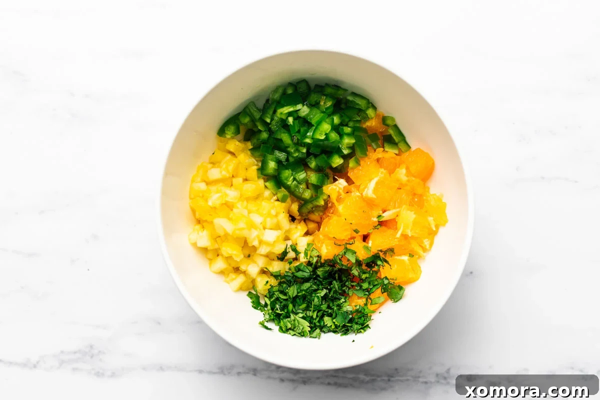 Exotic Flame-Grilled Chicken with Tropical Fruit Salsa 3 Close-up of freshly prepared, finely diced tropical salsa ingredients: golden pineapple chunks, vibrant orange segments, bright green cilantro, and minced red jalapeño.