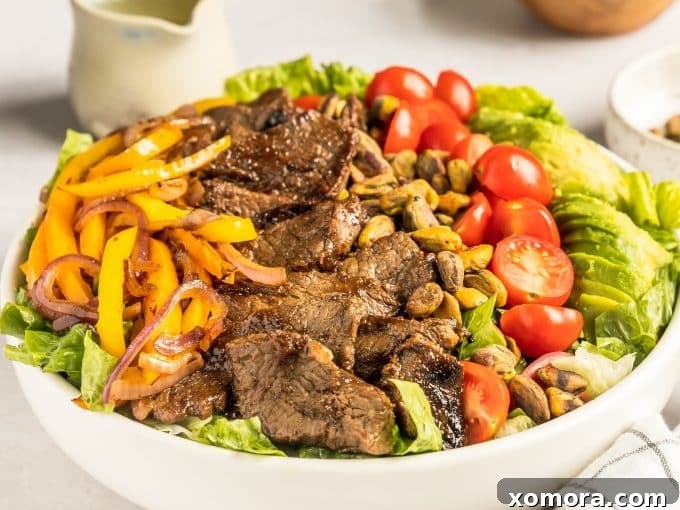 Fiesta Steak Salad with Citrus Vinaigrette 3 Ingredients for Southwestern Steak Salad laid out on a table, including sliced steak, colorful peppers, onion, avocado, tomatoes, and a small bowl of lime vinaigrette.