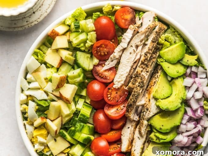 A close-up of a bowl of Lemon Chicken Cobb Salad, highlighting the variety of ingredients like chicken, avocado, hard-boiled eggs, and fresh greens, all glistening with the homemade lemon vinaigrette.