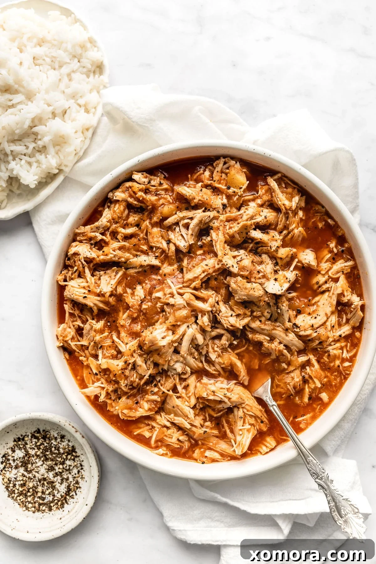 Slow Cooker Tropical Pulled Chicken 6 An overhead shot of Slow Cooker Pineapple Chicken served in a bowl, garnished with fresh cilantro and lime wedges.