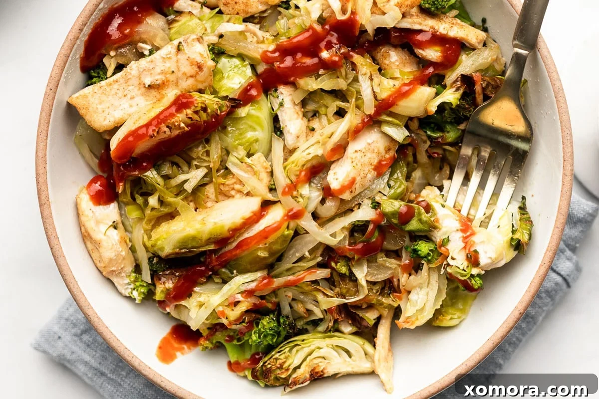 A close-up of a sheet pan filled with raw chicken, shredded cabbage, broccoli, Brussels sprouts, and onion, ready for the oven.