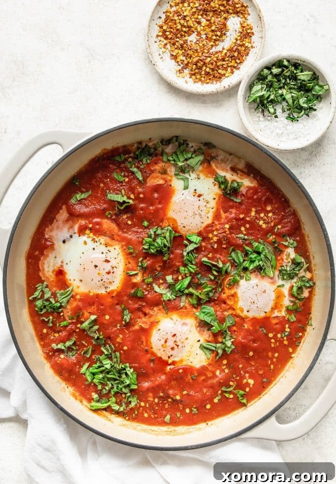 A vibrant pan of Shakshuka with perfectly poached eggs in rich tomato sauce, garnished with fresh herbs.
