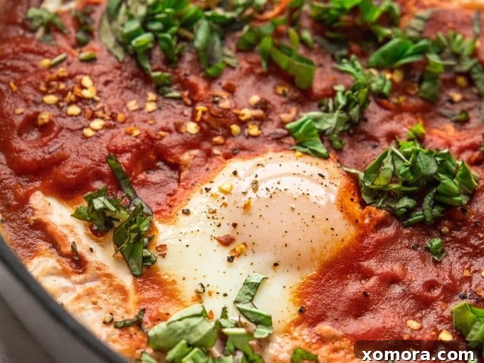 Close-up of the simmering tomato sauce with a spoon making a well for an egg in a cast iron skillet.