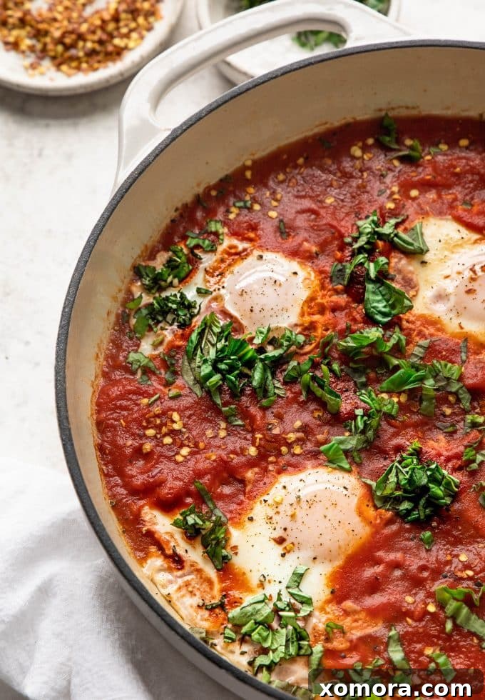A perfectly cooked Shakshuka in a black pan with fresh herbs and crumbled feta cheese on top, ready to be served.