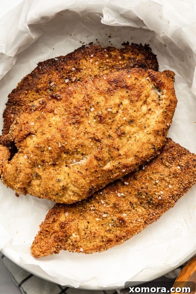 Crispy Almond Chicken Cutlets 4 A close-up of a golden-brown almond flour chicken cutlet being pan-fried in a cast iron skillet.