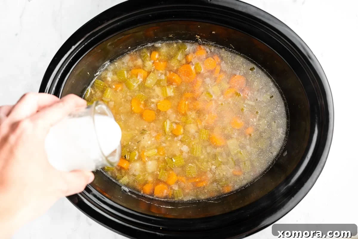 Comforting Crockpot Chicken Stew 4 A serving of slow cooker chicken stew in a white bowl, garnished with fresh herbs.