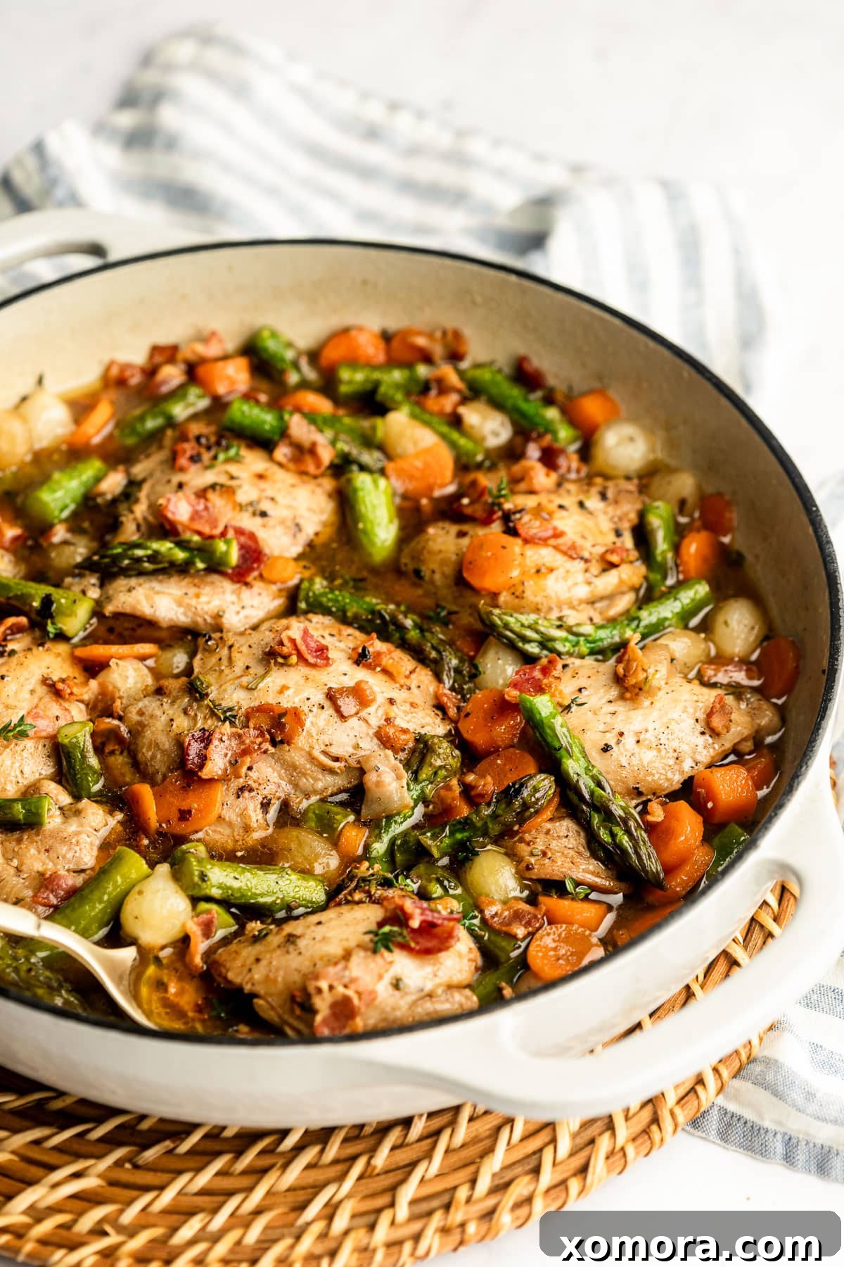 A skillet filled with beautifully seared chicken thighs, carrots, pearl onions, and fresh herbs.