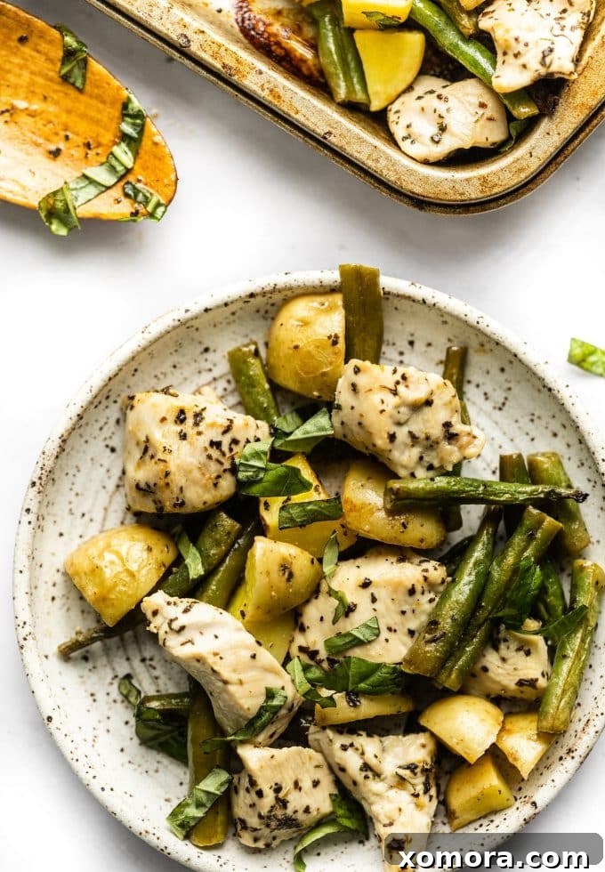 Close-up shot of seasoned chicken, green beans, and potatoes on a sheet pan, drizzled with olive oil and lemon juice.