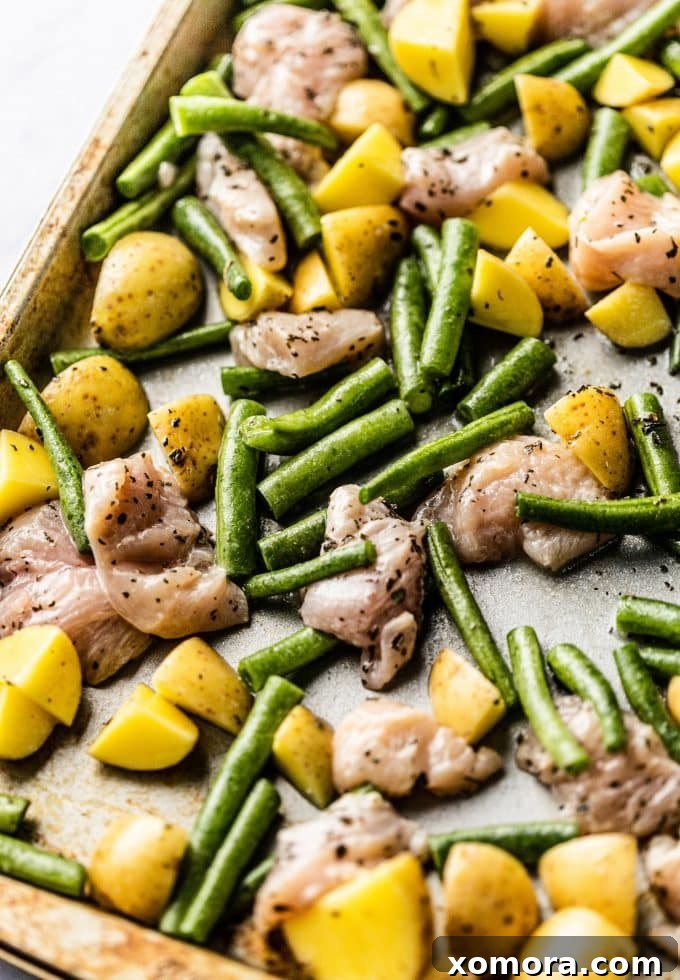 A close-up of roasted lemon chicken, green beans, and potatoes on a sheet pan, showing a golden brown finish.