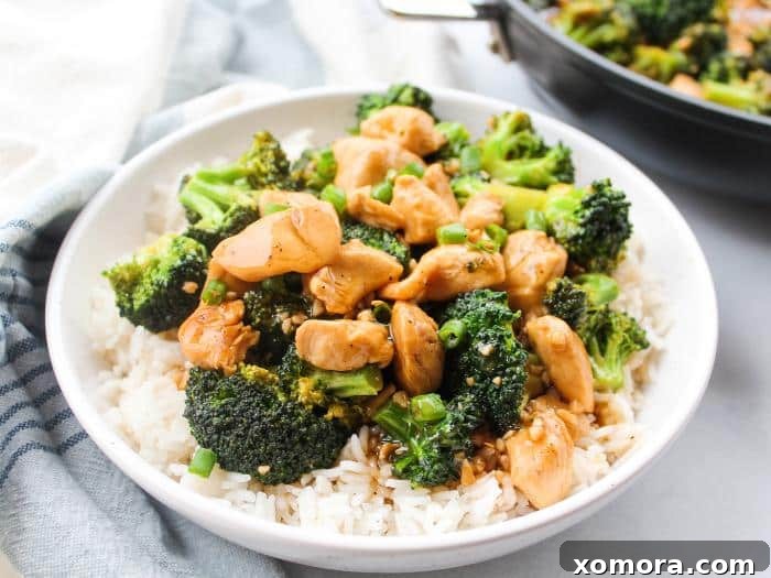 Savory Teriyaki Chicken and Broccoli Stir-Fry 3 A close-up of chicken chunks searing in a pan with broccoli florets being added to steam alongside.