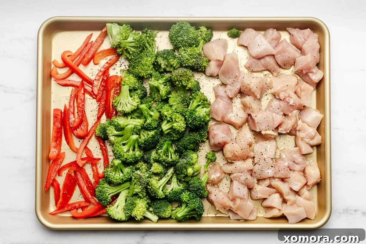 Effortless Sheet Pan Cashew Chicken 3 A sheet pan filled with diced chicken and broccoli florets, drizzled with olive oil and seasoning, ready for the oven.