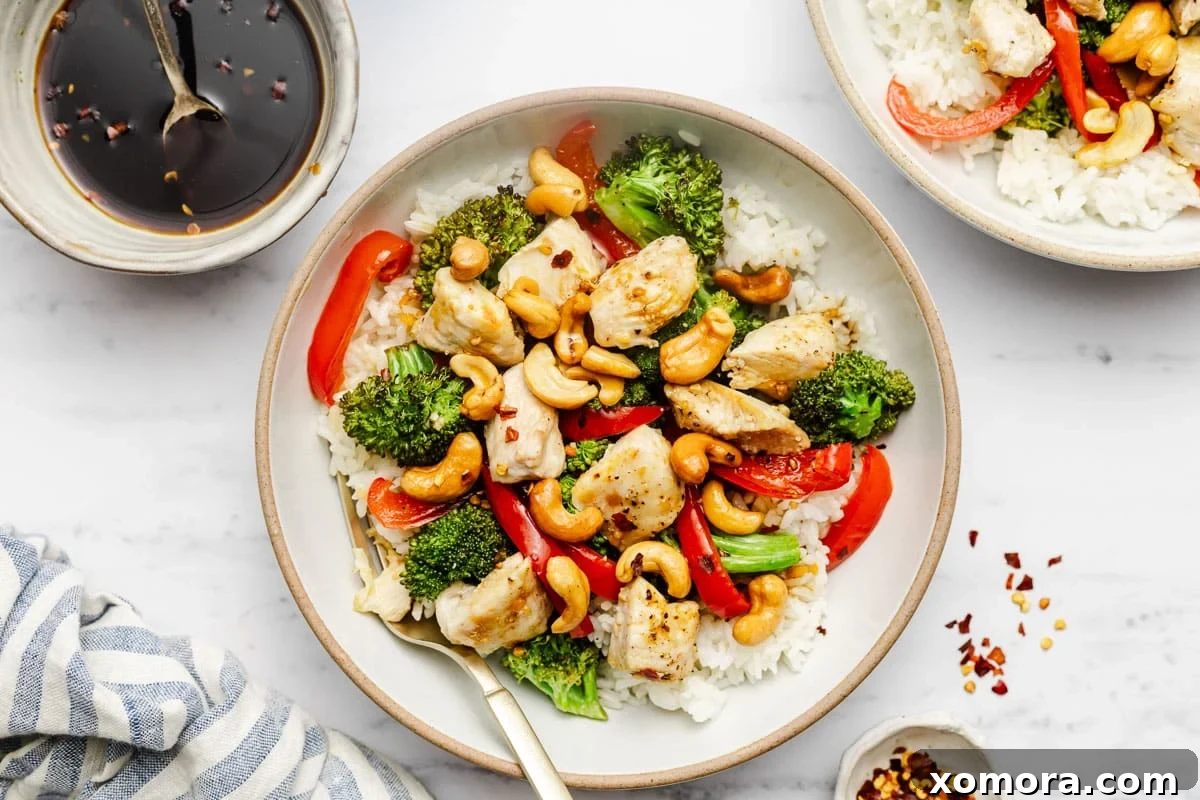 Effortless Sheet Pan Cashew Chicken 7 A serving of sheet pan cashew chicken in a bowl, with a fork, ready to eat.