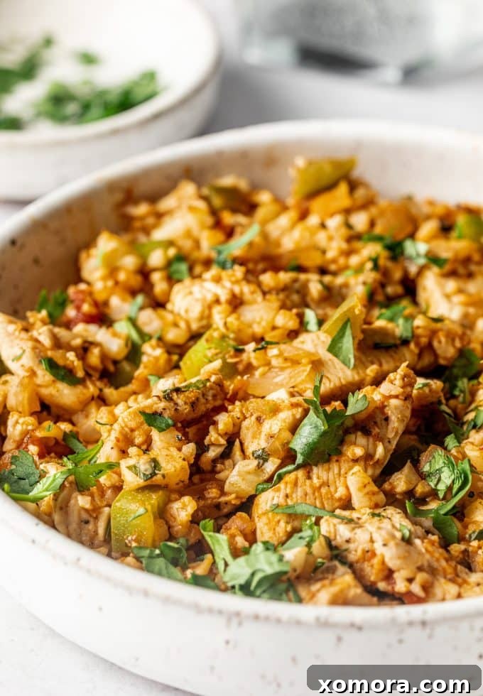 Fiesta Chicken Cauliflower Rice Skillet 2 Mexican Chicken Fried Cauliflower Rice in a skillet, garnished with fresh cilantro and avocado slices.