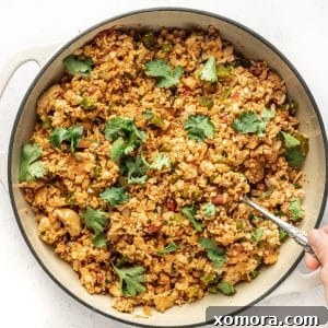 A vibrant bowl of Mexican Chicken Fried Cauliflower Rice, garnished with fresh toppings.