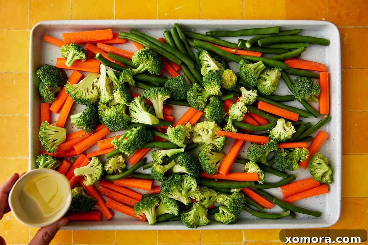 Ranch Roasted Vegetable Medley 3 A large baking sheet filled with a colorful mix of uncooked carrots, broccoli, and green beans, lightly drizzled with oil and seasonings